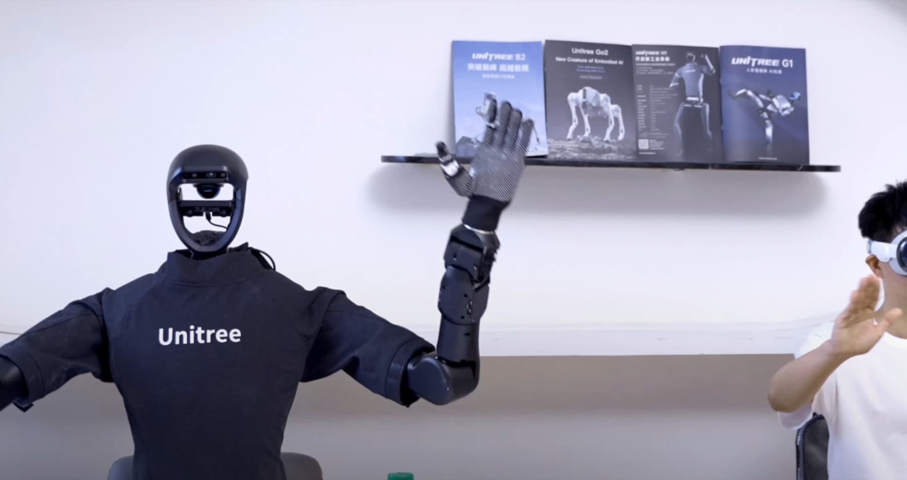 Operator wearing an XR headset and mirroring the raised hands of a Unitree G1 humanoid robot